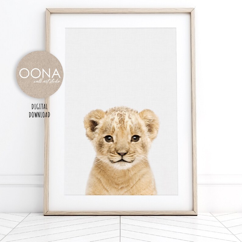 May include: A close-up of a lion cub with a light brown coat and big, brown eyes. The cub is looking directly at the camera with a sweet expression.