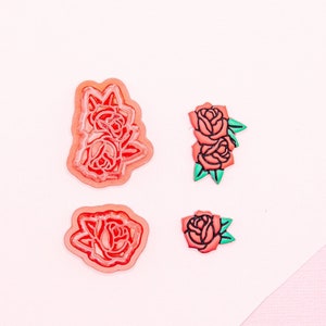 Könnte beinhalten: Vier rosa und grüne Rosenblüten-Aufkleber mit schwarzen Umrissen. Die Aufkleber befinden sich auf einem weißen Hintergrund.