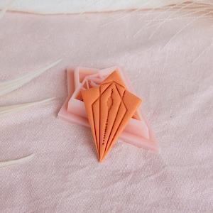 Puede incluir: Un molde de silicona de color melocotón en forma de estrella con un molde de silicona naranja más pequeño en forma de diamante en su interior.