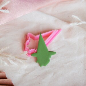 May include: A set of two pink and green plastic cookie cutters shaped like a witch's hat and a witch's face.