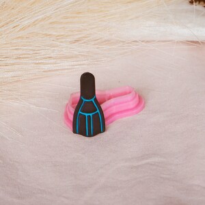 May include: A black and blue silicone mold shaped like a pair of scuba flippers. The mold is sitting on a pink surface.
