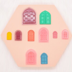 May include: A silicone mold with various sizes and shapes of arched windows, including a large arched door with a decorative design. The mold is pink and the windows are in various colors, including red, orange, yellow, green, blue, and purple.