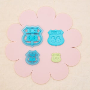 Puede incluir: Cuatro cortadores de galletas de plástico azul y verde con forma de señales de la Ruta 66. El cortador más grande es azul y dice "ROUTE 66" en letras blancas. Los otros tres cortadores son más pequeños y dicen "ROUTE 66" en letras blancas.