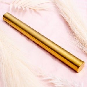 May include: A gold metal tube on a pink background with white fluffy stems.