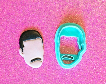 May include: Two cookie cutters, one blue and one white, shaped like a person's face with a mustache.