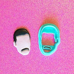 May include: Two cookie cutters, one blue and one white, shaped like a person's face with a mustache.