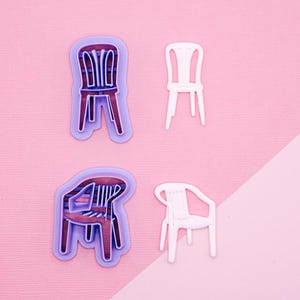Op de afbeelding: Vier plastic koekjesvormen in de vorm van stoelen, twee zijn wit en twee zijn paars. De witte vormen zijn eenvoudige ontwerpen, terwijl de paarse vormen een meer gedetailleerd ontwerp hebben.