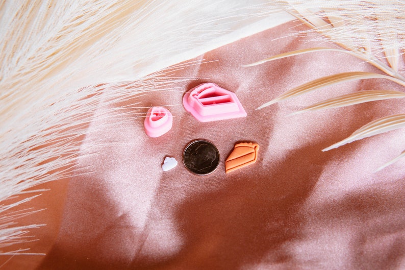 Puede incluir: Un conjunto de cinco cortadores de galletas de pl&aacute;stico rosa y naranja con forma de coraz&oacute;n, una rebanada de pastel, una tarta y un coraz&oacute;n peque&ntilde;o. Los cortadores est&aacute;n sobre un fondo rosa y blanco.