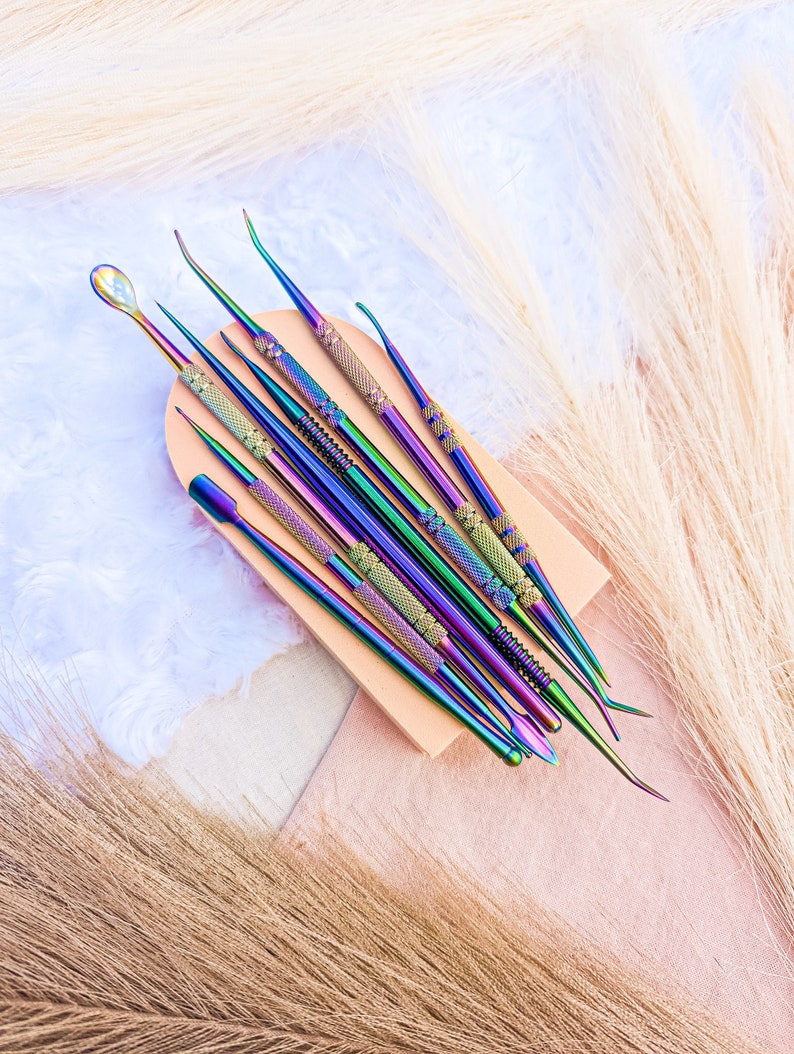 May include: A set of nine iridescent metal tools with different shaped tips, arranged on a wooden block. The tools are used for nail art and cuticle care.