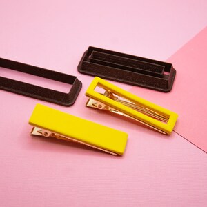 May include: Two yellow plastic hair clips with gold metal clasps and two brown plastic molds for making hair clips.