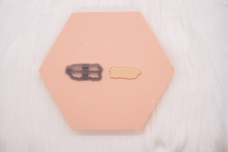 May include: Two cookie cutters, one in the shape of Puerto Rico with a black outline and the other in the shape of the Puerto Rican flag with a silver outline.