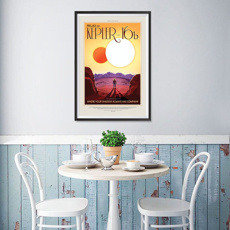 Puede incluir: Un p&oacute;ster enmarcado con un dise&ntilde;o de p&oacute;ster de viaje retro. El p&oacute;ster presenta un sol rojo y blanco, un paisaje rocoso y una figura solitaria de pie en primer plano. El texto en el p&oacute;ster dice: "Relax on Kepler-16b. The Land of Two Suns. Where your shadow always has company."