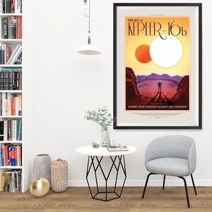 Puede incluir: Un p&oacute;ster enmarcado con un dise&ntilde;o de p&oacute;ster de viaje retro que presenta un sol rojo y blanco, un paisaje rocoso y una figura solitaria con un traje espacial. El texto en el p&oacute;ster dice "Relax on Kepler-16b, The Land of Two Suns, Where your shadow always has company."