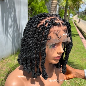 May include: A black, short-length wig with thick, textured locs. The wig is styled on a mannequin head, showcasing the intricate braiding and natural-looking hairline. The wig is designed to be worn by anyone.