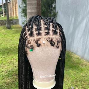 Peut inclure: Perruque noire tressée avec une dentelle frontale et une tête de mannequin. La perruque est coiffée en tresses carrées avec de longues tresses droites. La perruque est étiquetée "NeatCrowns".
