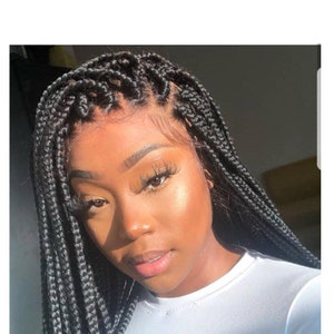 May include: A black braided wig with a lace front. The wig is styled in box braids and is worn by a person with dark skin.
