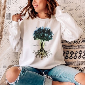 Puede incluir: Sudadera blanca con un dise&ntilde;o de &aacute;rbol de acuarela y las palabras "biophilia" y "spirit" en la parte delantera.