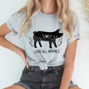 Puede incluir: Una camiseta gris con una ilustración en blanco y negro de un cerdo con flores y el texto "LOVE ALL ANIMALS".