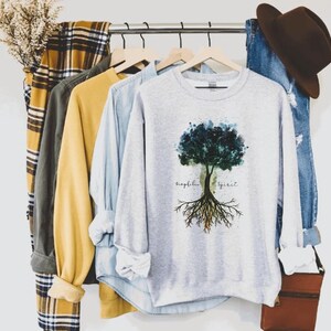 Puede incluir: Una sudadera gris con un dise&ntilde;o de &aacute;rbol de acuarela y el texto "biophilia spirit" impreso en la parte delantera.