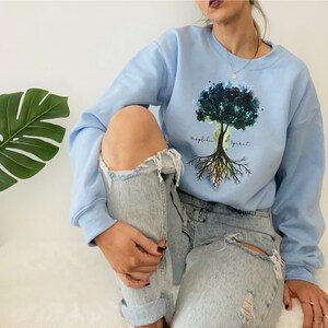 Puede incluir: Una sudadera azul claro con un dise&ntilde;o de &aacute;rbol de acuarela y el texto "biophilia spirit".