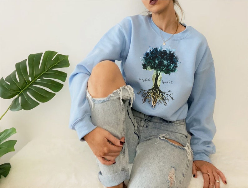 Puede incluir: Una sudadera azul claro con un dise&ntilde;o de &aacute;rbol de acuarela y el texto "biophilia spirit".