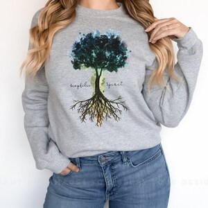 Puede incluir: Sudadera gris con un dise&ntilde;o de &aacute;rbol de acuarela. El &aacute;rbol tiene hojas verdes, azules y amarillas. Las ra&iacute;ces del &aacute;rbol est&aacute;n etiquetadas como "fr&aacute;gil" y "esp&iacute;ritu".