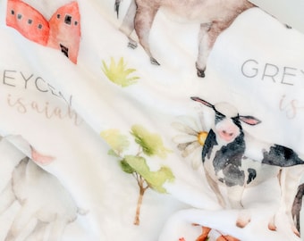 May include: A white baby blanket with a watercolor farm animal theme. The blanket features a donkey, a cow, a chicken, and a barn. The text "Grey is" and "Eyc isaiah" is printed on the blanket.