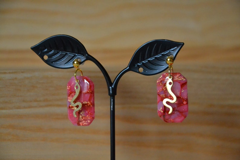 Peut inclure: Une paire de boucles d'oreilles roses et dor&eacute;es avec un motif de serpent. Les boucles d'oreilles sont en r&eacute;sine et ont une finition dor&eacute;e.