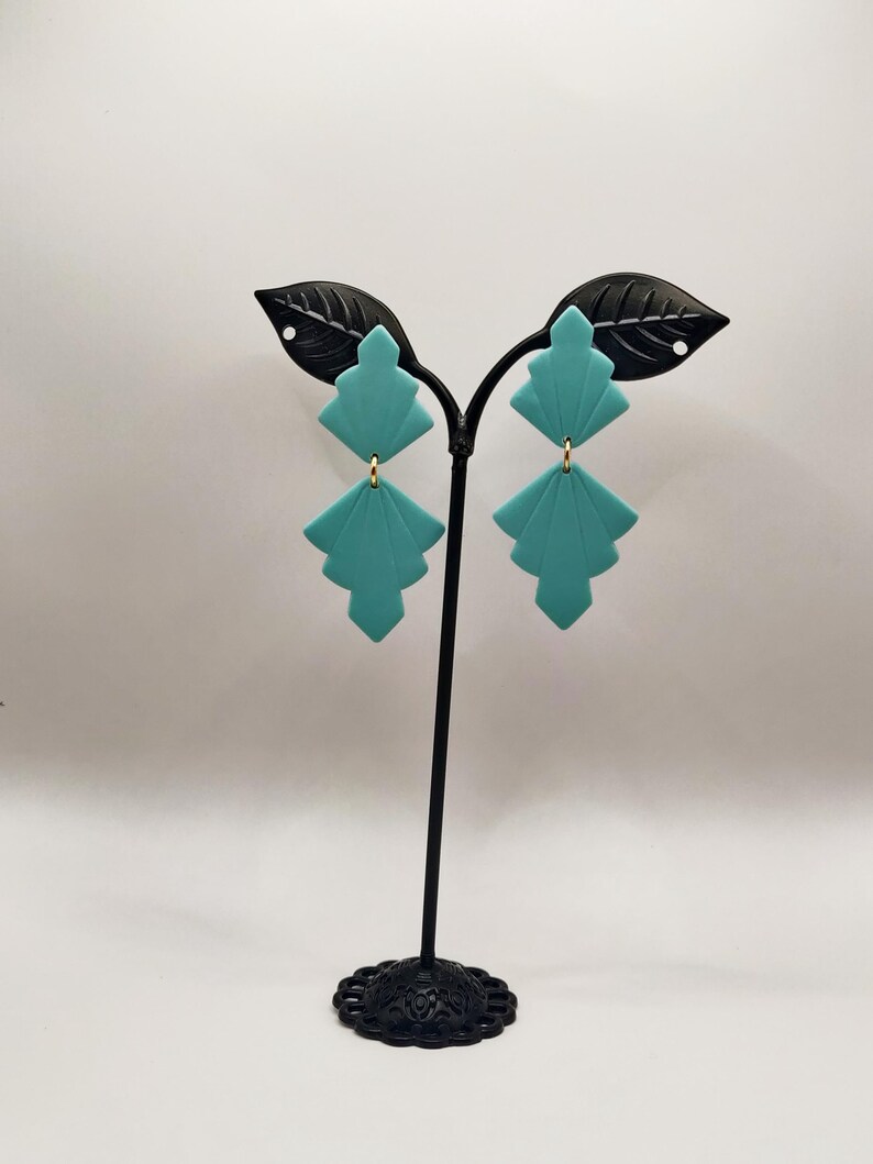 Peut inclure: Une paire de boucles d'oreilles g&eacute;om&eacute;triques bleu turquoise avec des accents dor&eacute;s sur un support de boucles d'oreilles noir.