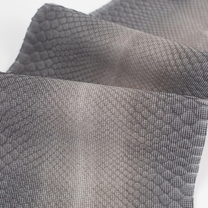 Könnte beinhalten: Nahaufnahme eines strukturierten Stoffes mit einem schuppenartigen Muster in Grautönen. Der Stoff ist gefaltet und zeigt die Textur und Farbvariationen. Das Material scheint weich und geschmeidig zu sein.