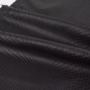 Op de afbeelding: Zwart slangenleer met een textuur, schubbenpatroon. Het leer is gevouwen en gedrapeerd, waardoor de natuurlijke nerf en textuur zichtbaar zijn.