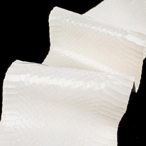 Op de afbeelding: Witte slangenleer met een textuur, schubbige oppervlak. Het leer is gevouwen en gedrapeerd, wat de zachte, soepele textuur laat zien.