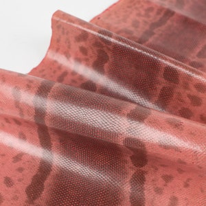 Könnte beinhalten: Nahaufnahme eines Stücks rotes Schlangenleders mit einem strukturierten Muster. Das Leder ist gefaltet und hat eine glänzende Oberfläche.