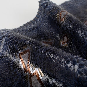 Puede incluir: Primer plano de una piel de serpiente azul oscuro con un patrón geométrico en plata y cobre.