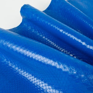 Puede incluir: Primer plano de un trozo de cuero de serpiente azul. El cuero está doblado y tiene un acabado brillante.
