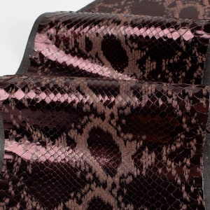 May include: A close-up of a dark brown snakeskin fabric with a subtle iridescent sheen. The fabric has a textured surface that resembles snake scales.