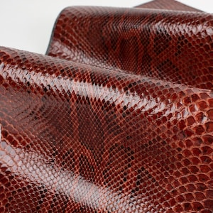 May include: Close-up of a brown snakeskin leather with a textured pattern. The leather is smooth and shiny.