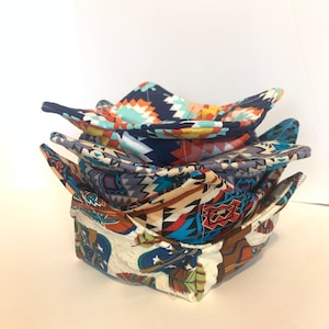 May include: A stack of four fabric bowl cozies in various geometric patterns. The cozies are made of cotton fabric and are designed to protect bowls from heat and scratches.