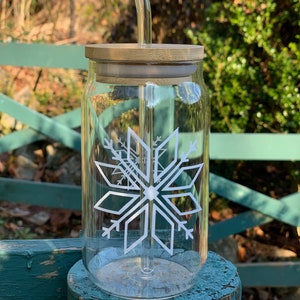 May include: A clear glass jar with a wooden lid and a glass straw. The jar has a white snowflake design on the front.