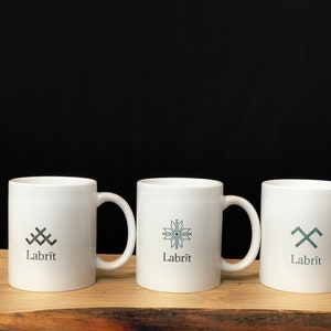 May include: Three white ceramic mugs with black and gray geometric designs and the word "Labrit" printed on the front.