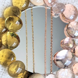 May include: A close-up of six different gold and rose gold chains hanging in front of a mirror. The chains are all different styles and thicknesses. The chains are surrounded by clear glass stones.