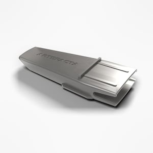 May include: A matte grey, wedge-shaped plastic component featuring the embossed text ARTEFACTA on its top surface. The object has a hollow, open-ended design with a tapered profile and structural ridges along its sides and base.