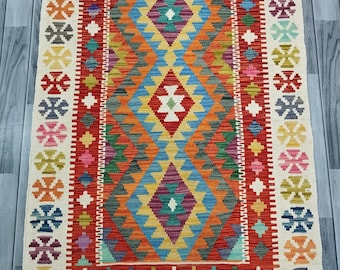 May include: A colorful rug with a geometric pattern in shades of red, blue, green, yellow, and white. The rug has a white border with a repeating floral design.