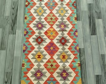 May include: A rectangular, hand-woven rug with a geometric diamond pattern. The rug features a vibrant color palette of red, orange, teal, yellow, purple, and gray. The rug's design is symmetrical, with a repeating pattern across its surface.