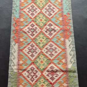 May include: A colorful rug with a geometric pattern in shades of red, orange, green, blue, and white. The rug has a fringe border.