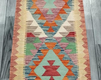 May include: A colorful geometric patterned rug with a cream background and red, orange, blue, green, and brown accents. The rug has a fringe border.