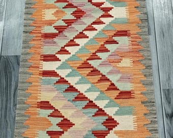 May include: A colorful geometric patterned rug with a fringe border. The rug is woven with shades of orange, red, green, and white.