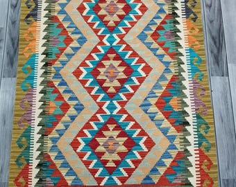 May include: A colorful rug with a geometric pattern in shades of red, blue, green, and yellow. The rug has a fringe border and is made of wool.