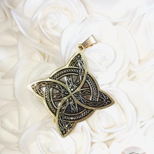 Peut inclure: Un pendentif doré avec un motif de nœud celtique. Le pendentif présente un motif complexe et entrelacé en noir et or. Le fond est un lit de roses blanches.