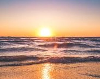 May include: A scenic photograph of a beach at sunset. The sky transitions from a deep blue at the top to vibrant orange and yellow near the horizon. The sun is a bright orb, reflecting on the ocean waves and wet sand.
